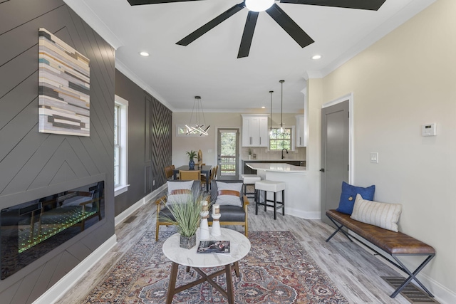 living room featuring ceiling fan, sink, light hardwood / wood-style flooring, a fireplace, and ornamental molding