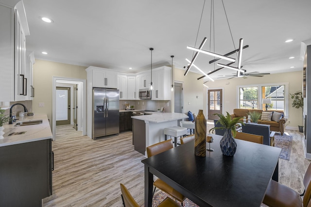 dining space featuring sink, light hardwood / wood-style floors, and ceiling fan with notable chandelier