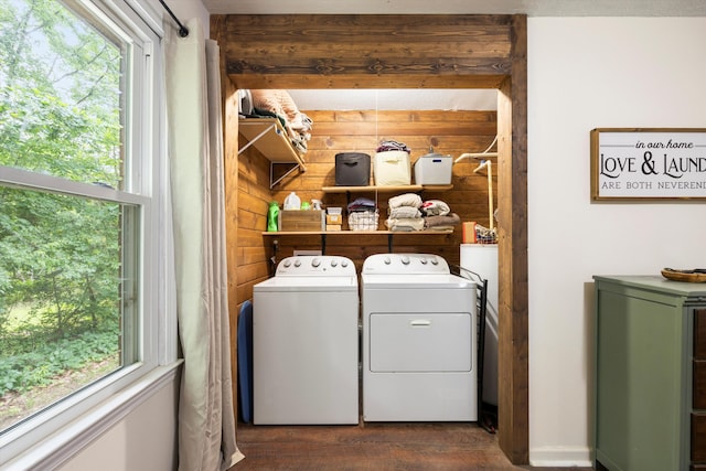 laundry area with wooden walls, washer and clothes dryer, a healthy amount of sunlight, and dark hardwood / wood-style floors