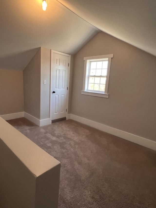 additional living space featuring lofted ceiling and dark colored carpet