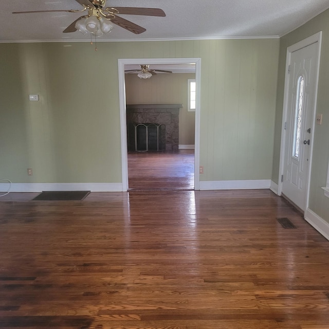 foyer featuring crown molding, dark hardwood / wood-style floors, a stone fireplace, and a textured ceiling