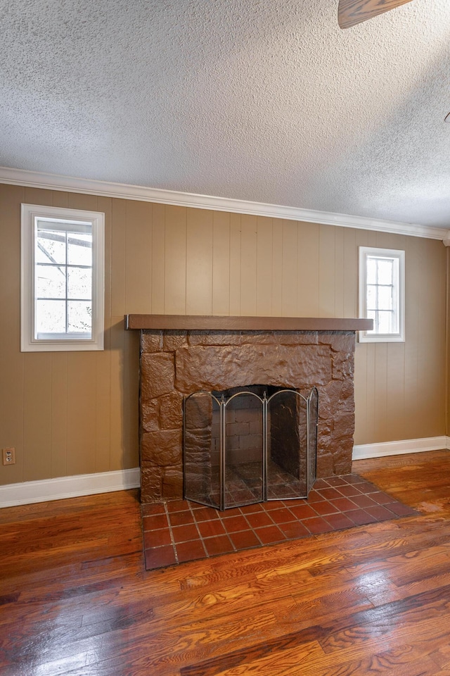 room details featuring a textured ceiling, a stone fireplace, wood walls, hardwood / wood-style flooring, and crown molding