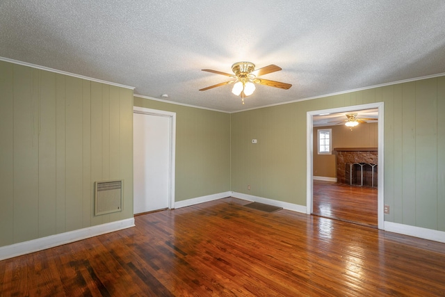 unfurnished room with ceiling fan, a fireplace, wood-type flooring, a textured ceiling, and crown molding