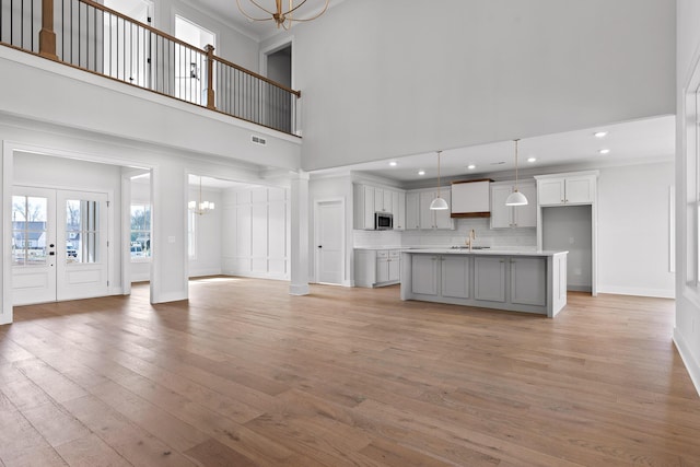 unfurnished living room with french doors, sink, ornamental molding, a towering ceiling, and light hardwood / wood-style floors