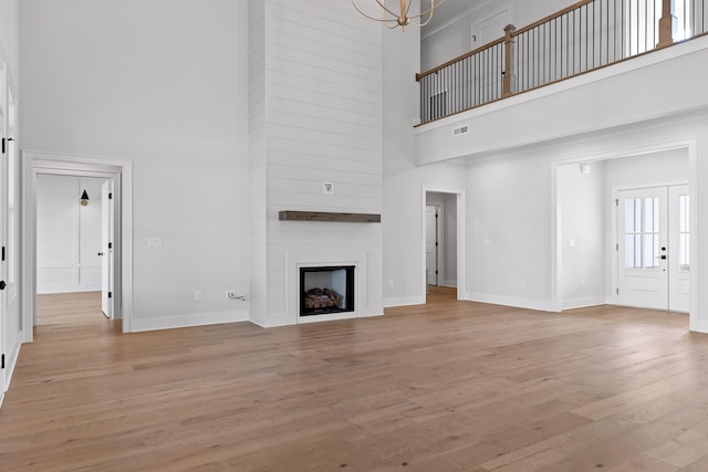 unfurnished living room with a fireplace, a towering ceiling, a notable chandelier, and light wood-type flooring