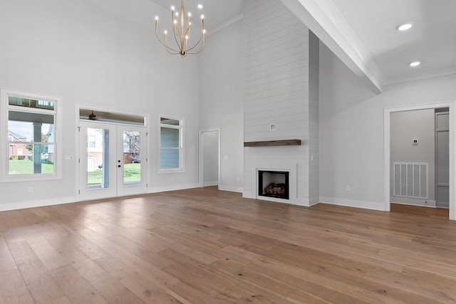 unfurnished living room with french doors, an inviting chandelier, ornamental molding, a fireplace, and light wood-type flooring