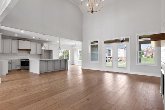 unfurnished living room featuring a high ceiling, french doors, sink, light hardwood / wood-style floors, and a chandelier