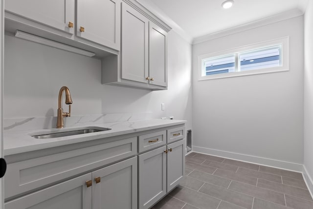 clothes washing area featuring cabinets, ornamental molding, and sink