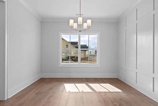 unfurnished dining area featuring light hardwood / wood-style flooring, ornamental molding, and a notable chandelier