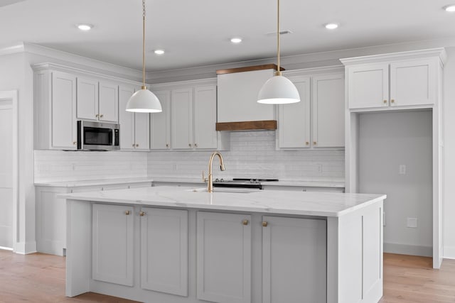 kitchen with light stone countertops, a center island with sink, white cabinetry, and hanging light fixtures