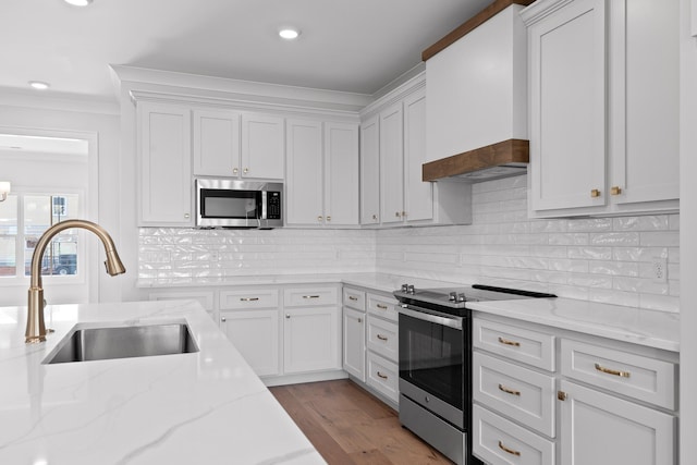 kitchen featuring white cabinetry, sink, light stone counters, custom range hood, and appliances with stainless steel finishes