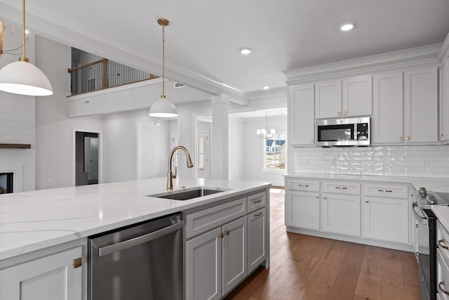 kitchen with light stone countertops, a large fireplace, stainless steel appliances, sink, and hanging light fixtures