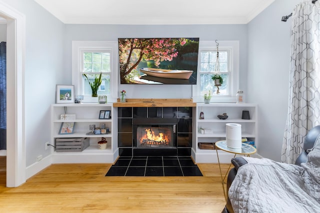 living room with a tiled fireplace, a healthy amount of sunlight, crown molding, and wood-type flooring