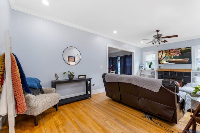 living room with a tiled fireplace, ceiling fan, light hardwood / wood-style flooring, and ornamental molding