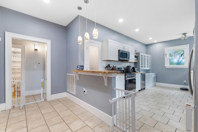 kitchen featuring a breakfast bar, white cabinets, hanging light fixtures, decorative backsplash, and appliances with stainless steel finishes