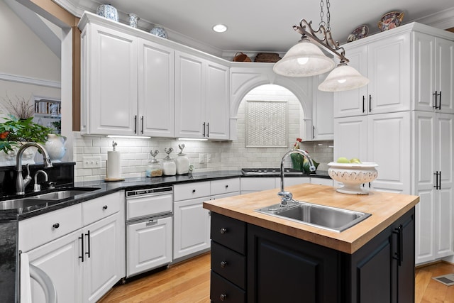 kitchen with butcher block counters, a kitchen island with sink, sink, and white cabinets