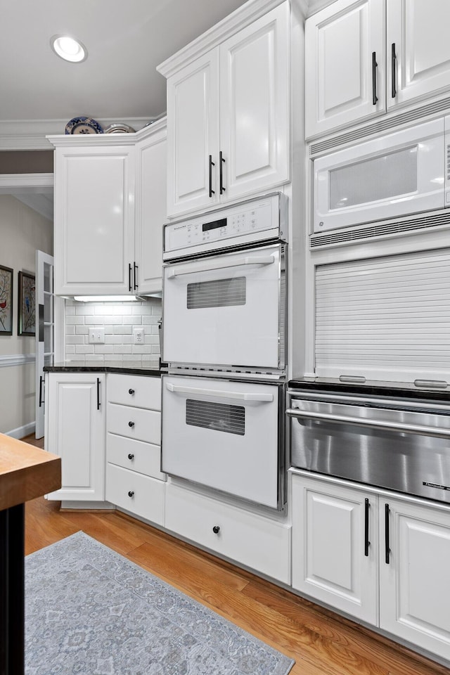 kitchen featuring white appliances, backsplash, ornamental molding, light hardwood / wood-style floors, and white cabinetry