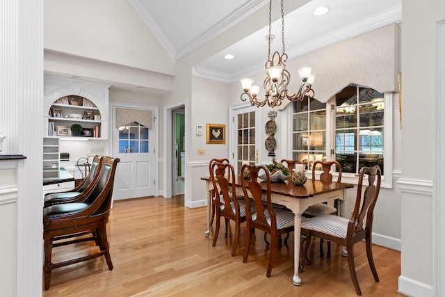 dining room featuring light wood-type flooring, ornamental molding, built in shelves, vaulted ceiling, and a notable chandelier