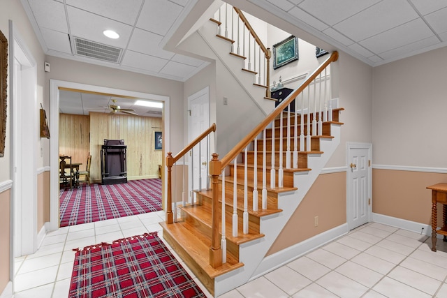 staircase featuring a drop ceiling, tile patterned floors, ceiling fan, and wood walls