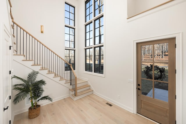 entryway with a healthy amount of sunlight, light wood-type flooring, and a towering ceiling