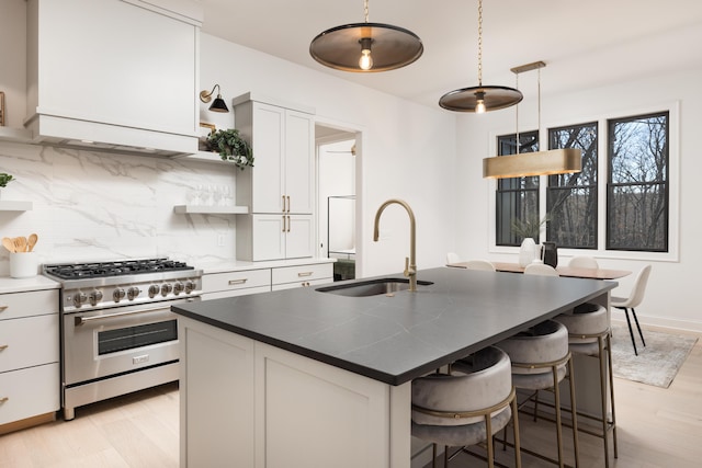 kitchen featuring high end range, a kitchen island with sink, white cabinets, hanging light fixtures, and decorative backsplash