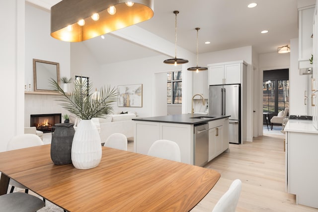 kitchen featuring white cabinetry, stainless steel appliances, decorative light fixtures, a kitchen island with sink, and light wood-type flooring