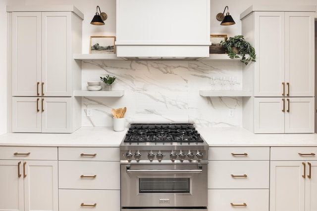 kitchen featuring white cabinets, tasteful backsplash, high end stainless steel range oven, and light stone countertops