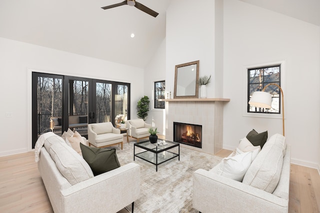 living room with french doors, ceiling fan, high vaulted ceiling, a fireplace, and light hardwood / wood-style floors