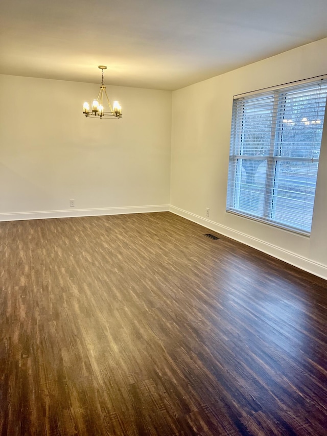 empty room featuring dark wood-type flooring and a chandelier