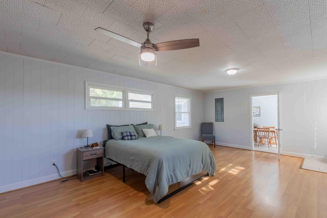 bedroom featuring wood walls, electric panel, ceiling fan, ornamental molding, and light hardwood / wood-style floors