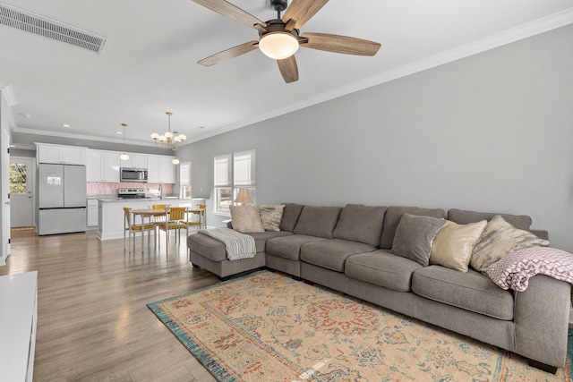 living room featuring ceiling fan with notable chandelier, light hardwood / wood-style flooring, crown molding, and sink