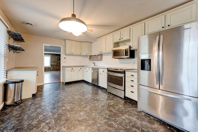 kitchen with decorative backsplash, appliances with stainless steel finishes, brick wall, sink, and white cabinetry