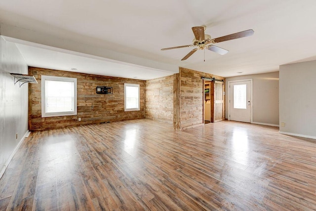 unfurnished living room featuring a barn door, hardwood / wood-style flooring, and ceiling fan