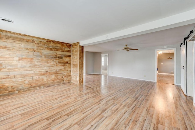 unfurnished room featuring ceiling fan, a barn door, beamed ceiling, wood walls, and light wood-type flooring