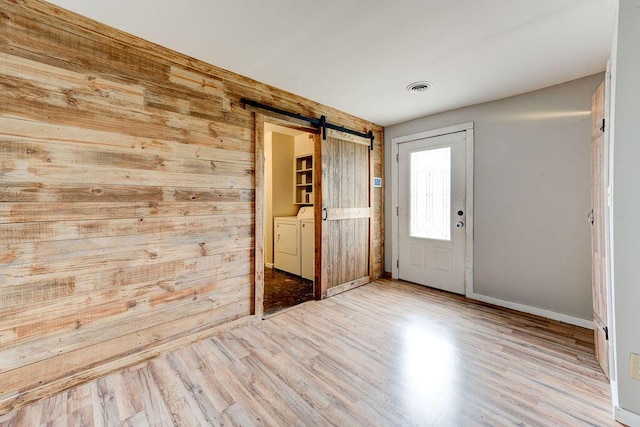 foyer with washing machine and clothes dryer, a barn door, wooden walls, and light hardwood / wood-style floors