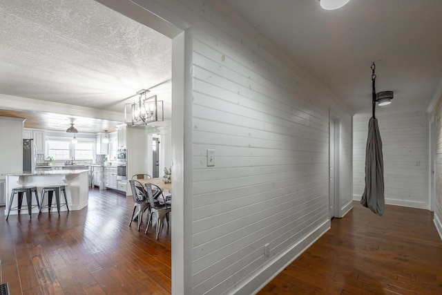 corridor with a chandelier, dark hardwood / wood-style flooring, wood walls, and a textured ceiling