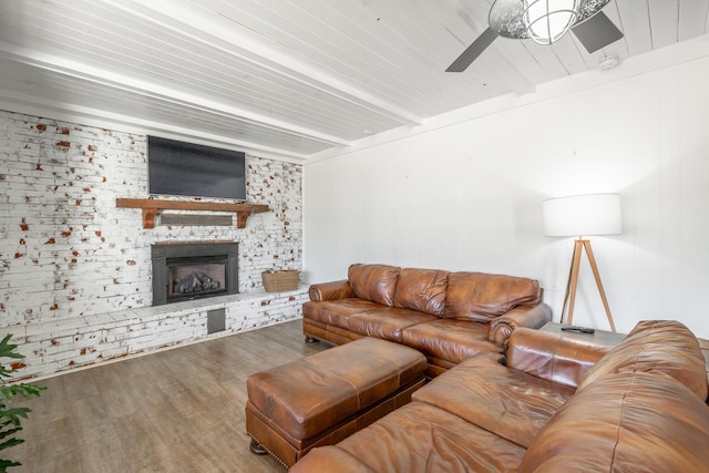 living room with hardwood / wood-style floors, brick wall, ceiling fan, a brick fireplace, and beam ceiling