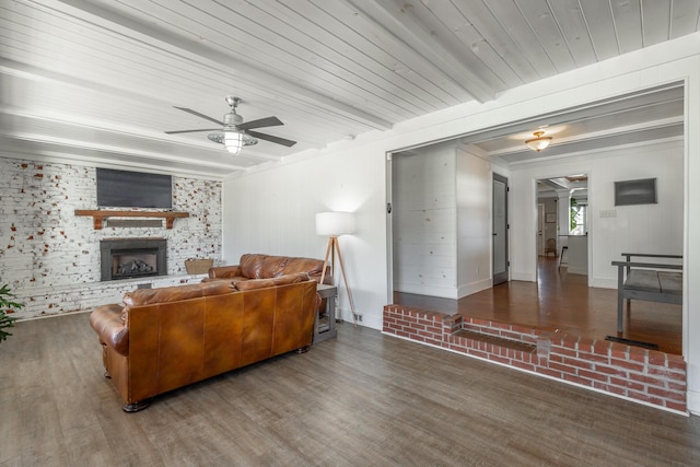 living room with ceiling fan, a fireplace, beamed ceiling, and dark hardwood / wood-style floors