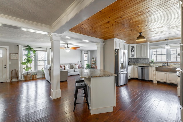 kitchen with white cabinetry, stainless steel appliances, a kitchen breakfast bar, ceiling fan, and light stone counters