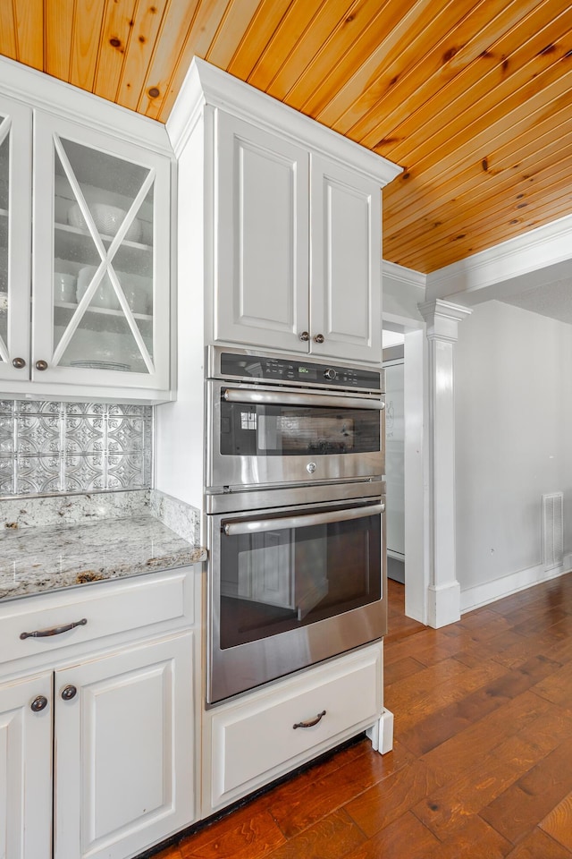 kitchen with light stone countertops, wooden ceiling, white cabinets, and stainless steel double oven