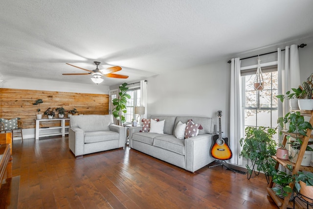 living room with ceiling fan, a textured ceiling, dark hardwood / wood-style floors, and wooden walls