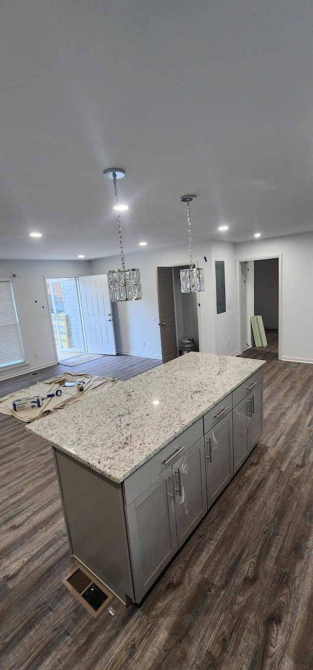 kitchen featuring a center island, dark hardwood / wood-style floors, gray cabinets, decorative light fixtures, and light stone counters