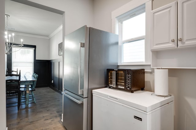 kitchen with an inviting chandelier, ornamental molding, fridge, white cabinetry, and stainless steel refrigerator