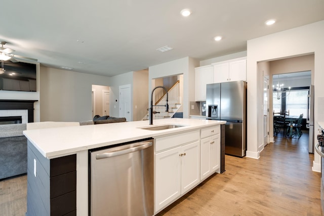 kitchen with ceiling fan with notable chandelier, sink, an island with sink, white cabinetry, and stainless steel appliances