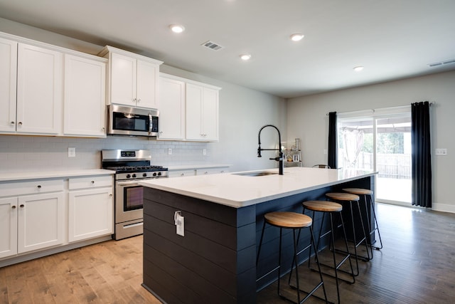 kitchen with a center island with sink, white cabinets, sink, light wood-type flooring, and appliances with stainless steel finishes