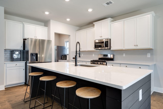 kitchen with white cabinets, stainless steel appliances, a center island with sink, and sink