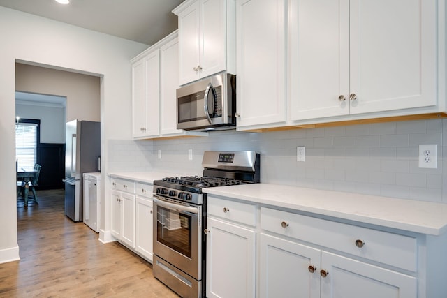 kitchen with light stone countertops, light hardwood / wood-style floors, decorative backsplash, white cabinets, and appliances with stainless steel finishes