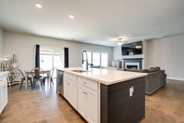 kitchen with sink, stainless steel dishwasher, an island with sink, white cabinets, and light wood-type flooring