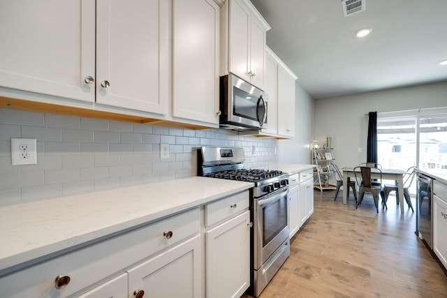 kitchen with tasteful backsplash, light stone counters, light hardwood / wood-style flooring, white cabinets, and appliances with stainless steel finishes