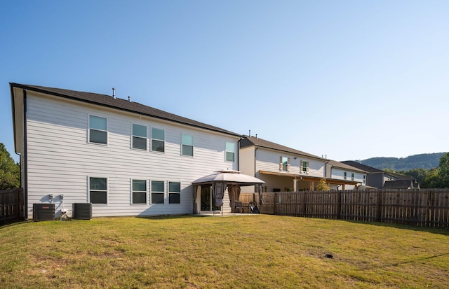 rear view of property featuring a gazebo, central air condition unit, and a lawn